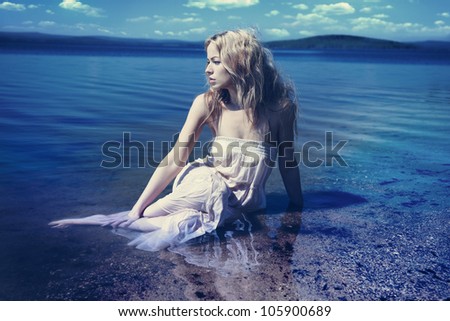 Young sexy blond woman in the blue water in wet white dress