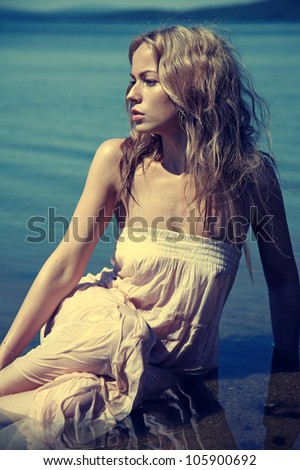 Young sexy blond woman in the blue water in wet white dress