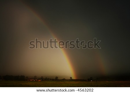 Large rainbow during thunderstorm over farmers field
