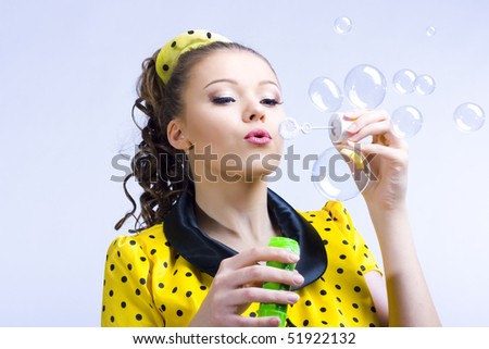 beautiful young woman blowing soap bubbles on blue background