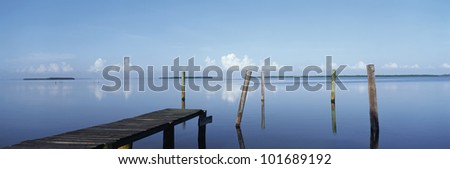 This is the morning view of Pine Island Sound. Its pier juts out from the left side with wooden pylons standing up out of the water near the shore.