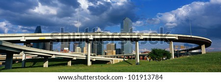 This is a freeway overpass with the Dallas skyline visible behind it. The freeway curves and snakes around in a circle in front of the city.