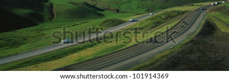 This is Route 580 at the Altamont Pass. There is green grass on each side of the highway with two separate roads for cars to travel in each direction.