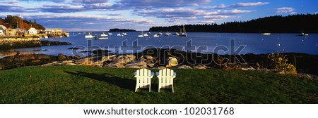 This is an image of two white lawn chairs facing toward the nearby harbor.