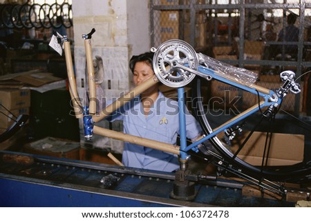 CIRCA 1999 - Woman on manufacturing assembly line holding bicycle