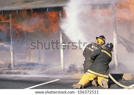 CIRCA 1999 - Two firefighters spraying burning building
