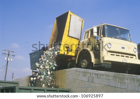 CIRCA 1988 - A recycling truck emptying the contents of a yellow bin