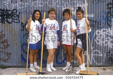 CIRCA 1990 - Four teenage girls participating in community cleanup on Clean and Green Day in East Los Angeles, California