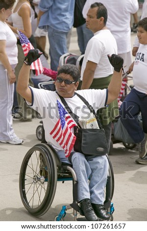 Man in wheel chair holds US flag in sympathy with immigrants participating in march for Immigrants and Mexicans protesting Illegal Immigration reform by U.S. Congress, Los Angeles, CA, May 1, 2006