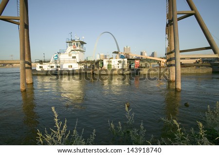 Towboat pushing barge down Mississippi River in front of Gateway Arch and skyline of St. Louis, Missouri as seen from East St. Louis, Illinois on the Mississippi River