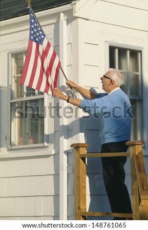STONINGTON, MAINE - CIRCA 1980\'s: Senior citizen raises the American flag on house in Stonington, Maine
