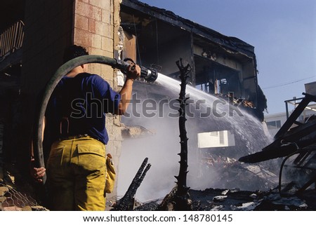 LOS ANGELES, CA - CIRCA 1992: Firefighter aiming hose at charred building after riots in Los Angeles, CA