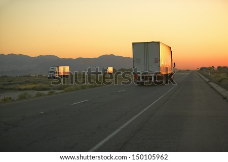 MOJAVE DESERT, CA - JULY 29: 18-wheeler semi-trucks at sunset hit the highway driving down Interstate Highway 15 between Los Angeles and Las Vegas Nevada on July 29, 2004 in Southern California