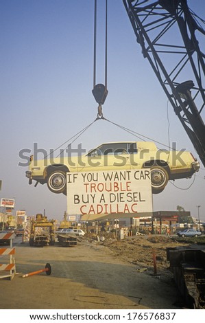 A lemon-yellow Cadillac, which lived up to its color, hangs from a crane near a service station. A sign warns future car purchasers away from this particular model. Hollywood, California