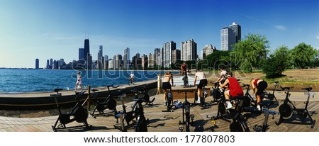 This is a spinning class taking place on North Avenue Beach at Lake Michigan. Several people are riding stationary bicycles with an instructor facing them in front. It signifies fitness, Chicago, IL.