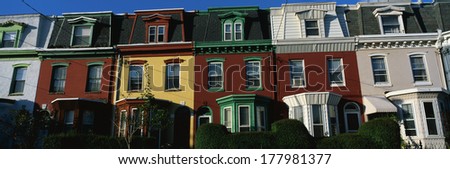 These are typical urban style row houses. They are all lined up next to each other with neatly trimmed bushes in front of them. They are colorfully painted in red, white or yellow paint.