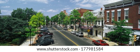 This Is The Eastern Shore Of Maryland. It Typifies Small Town America Or Main Street Usa. We See Shop Fronts On A Tree Lined Street. Cars Are Parked In Front Of Shops On Either Side Of The Street.