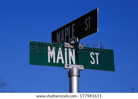 This is a street sign labeling the corner of Main Street & Maple Street. The sign is green with white lettering against a blue sky.