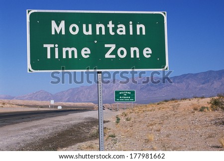 This is a road sign indicating a change to the Mountain Time Zone. The sign is green against a blue sky.