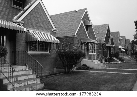 This is a black and white image of a row of single family houses. They are located on the south side of Chicago. They are brick houses with striped awnings over the front window and front door.