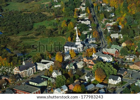 This is an aerial view of the New England village of Stowe. It is along scenic Route 100. There is autumn foliage in the trees. It is a typical looking small New England town.