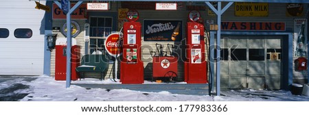 This is a vintage gas station with old style pumps that are red. It is a piece of Americana. It shows winter in New England.