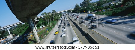 This is the Interstate 405 and 10 at rush hour. There are many cars lined up on the freeway with an overpass on the left hand side. There are a few houses to the right of the freeway.