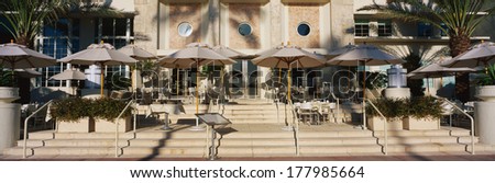 This is an outdoor cafe along the strip of South Beach Miami. There are umbrellas to shade customers from the sun with steps leading up to the cafe.
