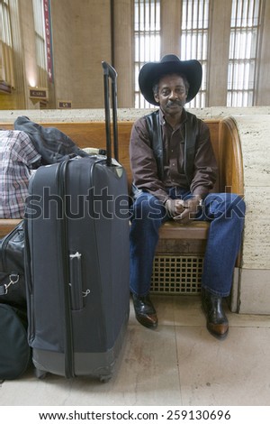 Black man with bags, cowboy hat and cowboy shoes waiting for train at 30th Street Station, AMTRAK Train Station in Philadelphia, PA