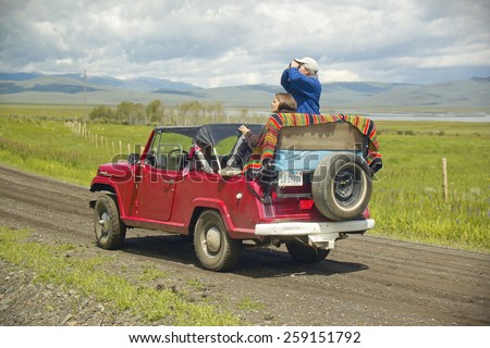 Bird watchers and red jeep in spring grasslands and mountains in Centennial Valley, Lakeview MT