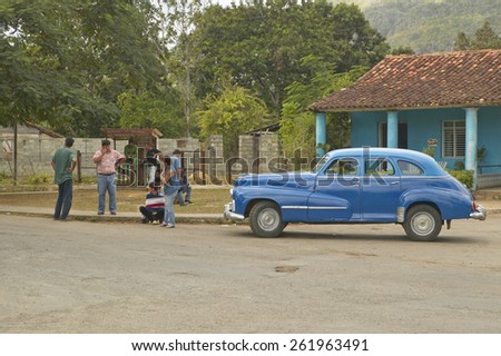 Old cars and three people in Cuban village in rural central Cuba