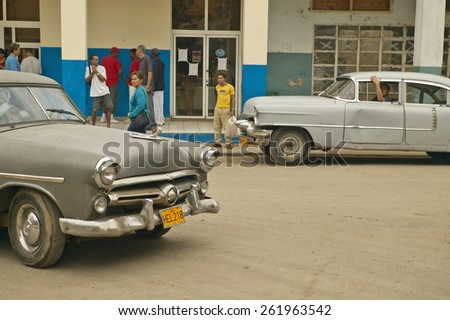Old cars in Cuban village near the El Rincon driving past old store and villagers