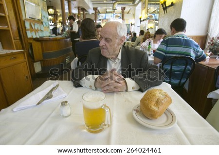 100 year old man sits down to a mug of beer and  a loaf of bread in a restaurant in Madrid, Spain