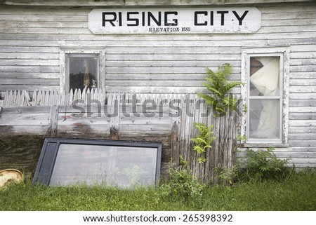 A rundown house with a sign on it\'s side that reads Rising City, Nebraska