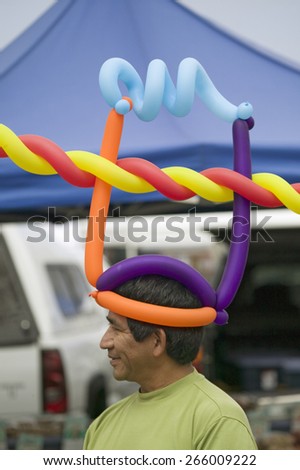 A Hispanic man wares multi-colored balloons on his head at farmers market in Santa Barbara California