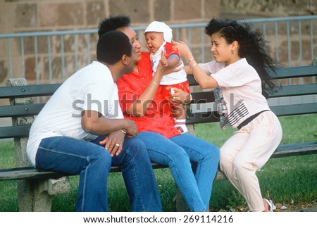An African-American family playing with a baby on a park bench, NY City