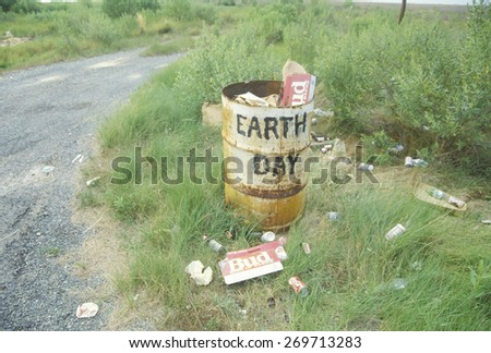 Cardboard beer cartons on the ground next to a trash can with the words Ã?Â??Earth DayÃ?Â?? painted on its side