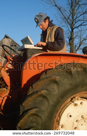 Farmer working on laptop computer on his tractor, Missouri