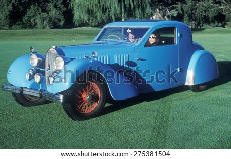 A man and woman in a blue Bugatti automobile at a vintage car show in Pebble Beach, California, ca. 1985.