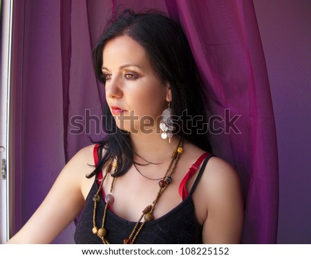 Beautiful brunette woman looking through the window and curtains