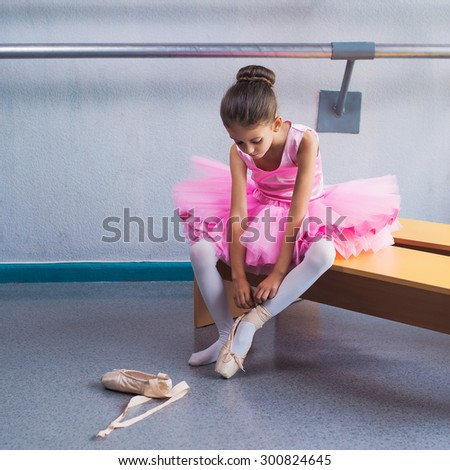Young ballerina in pink clothes sitting on the bench during the training in dance class.