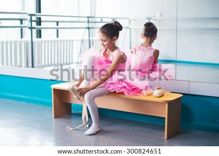 Young ballerina in pink clothes sitting on the bench during the training in dance class.