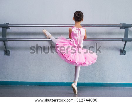 Young ballerina in a pink ballet tutu is dancing in dance class