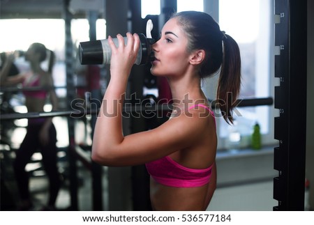 The sports young woman drinks protein cocktail in a shaker in a gym. Sports nutrition concept