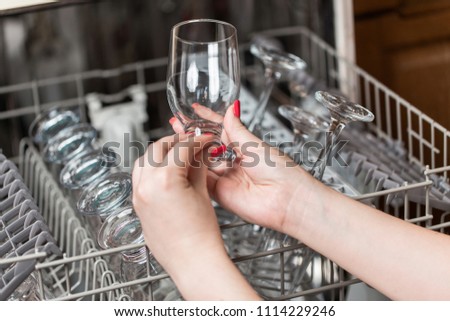 Close up shot of woman\'s hand taking out clean dishes from dishwasher machine.