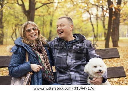 Happy middle aged couple sitting on park bench with their dog and smiling.