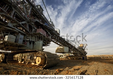 One side of huge mining drill machine photographed from a ground with wide angle lens. Dramatic and colorful sky in background.