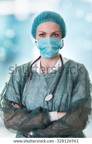 Closeup portrait of female doctor with stethoscope, bonnet and surgery mask on creamy blue background.