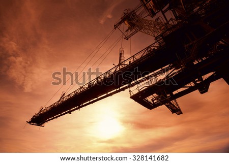 Silhouette of huge mining drill machine photographed from a ground with a wide angle lens into the sun. Dramatic and colorful red sky in background.