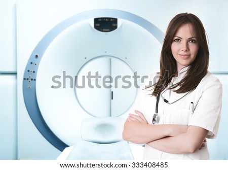 Indoor hospital portrait of beautiful female doctor with stethoscope standing, smiling and looking directly at the camera. In background is magnetic resonance scanner MRI.